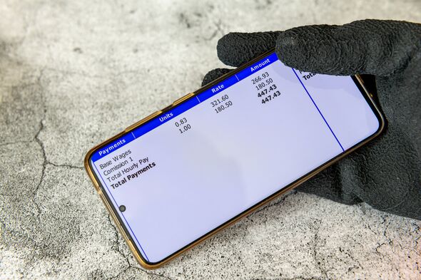 A worker wearing work gloves holding a smart phone with a digital pay slip of wage earnings.