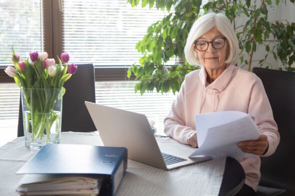 Senior woman reading document, using laptop computer