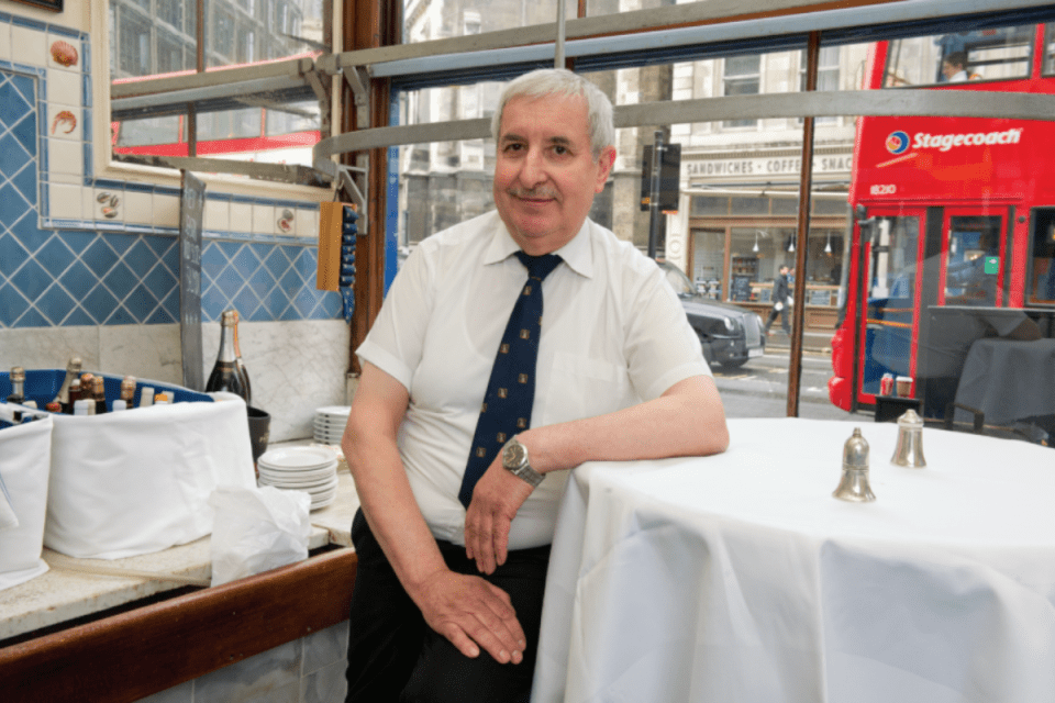 Sweetings City of London staff member with a red double-decker bus passing by outside.