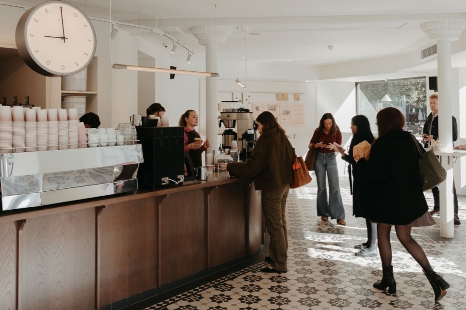 Customers and staff inside Rosslyn Coffee Ludgate Circus, with a large clock, coffee bar, and tiled floor.