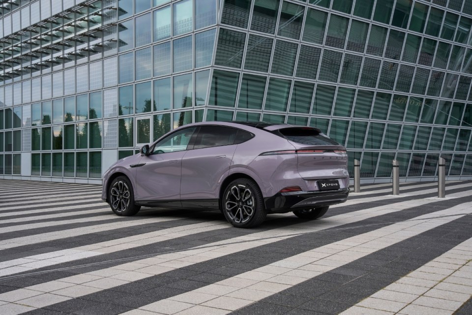 XPENG G6 electric SUV in light purple, parked on striped pavement in front of a modern glass building.