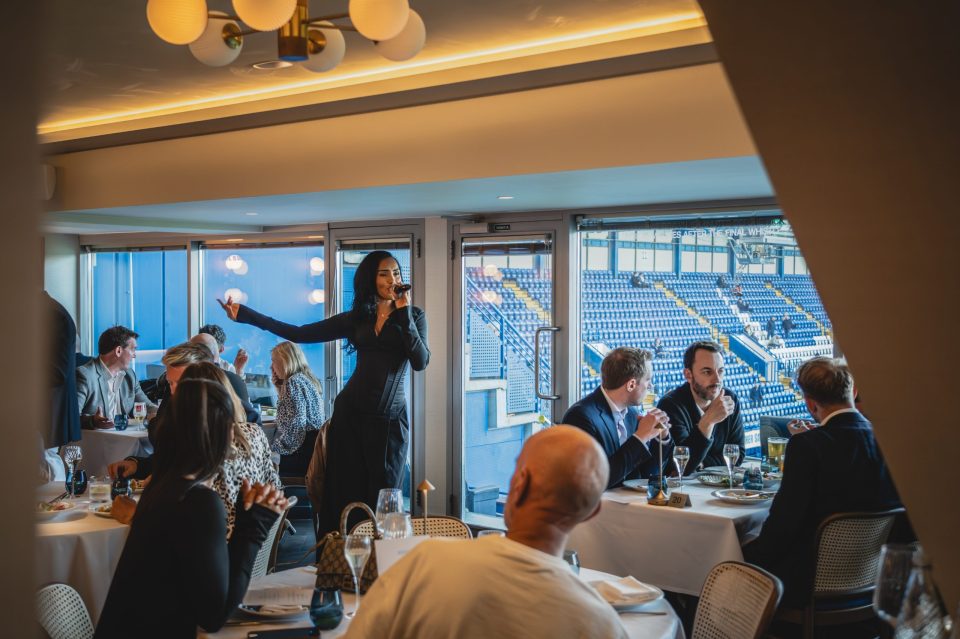Female singer performing at a corporate event with a stadium view, guests dining in foreground