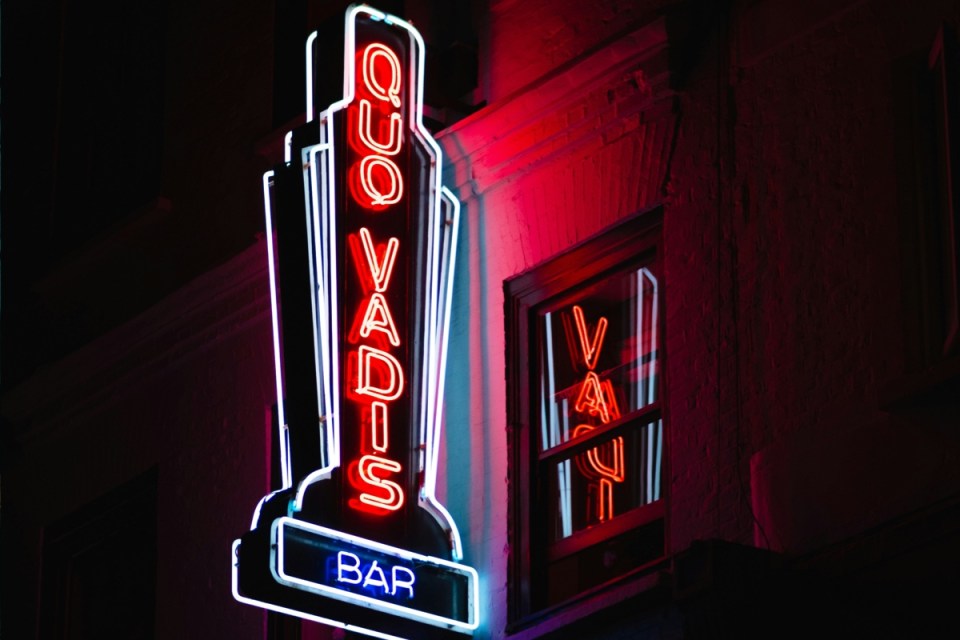 Neon sign for Quo Vadis Bar in Soho, London, illuminated red and blue at night.