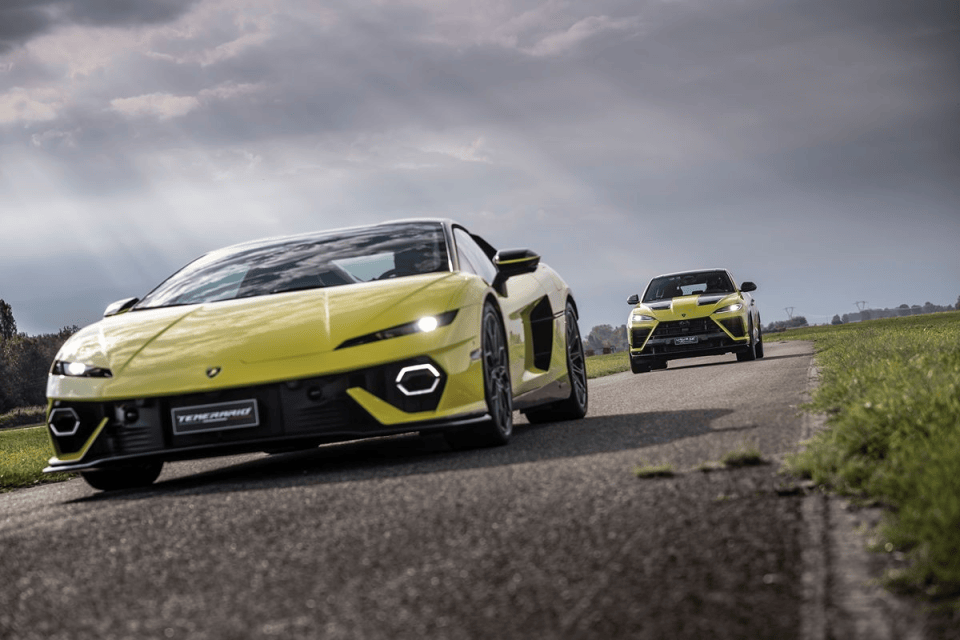 Two yellow Lamborghini supercars, a Huracán and Urus, on a winding road with green fields under a cloudy sky.
