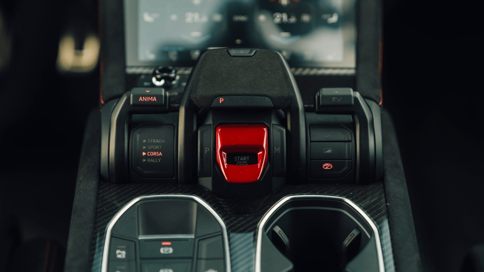 Luxury car interior with red start engine button, gear selector, and driving mode controls.