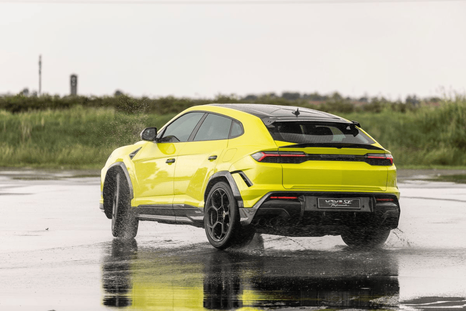Bright yellow Lamborghini Urus SE Performante SUV on a wet road, water splashing from tires.