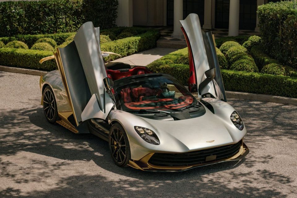 Luxury silver and gold sports car with open butterfly doors and red interior parked on a driveway.