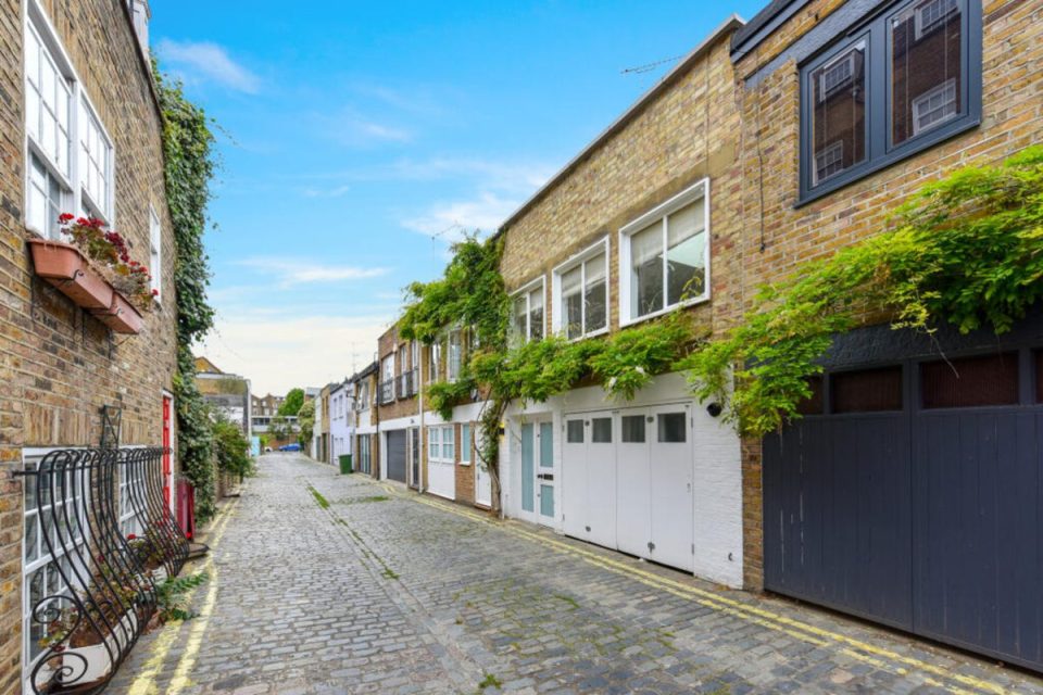 Cobblestone street in Notting Hill, London, lined with brick mews houses featuring garages and lush green ivy.