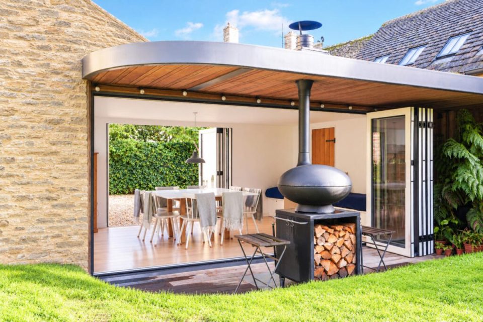 Outdoor living space at The Haven Oxfordshire with a modern fireplace, dining area, and lush garden views.