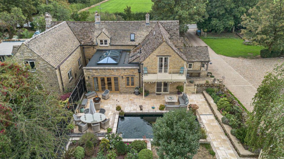 Aerial view of a large stone house in Burford with a patio, pool, and garden