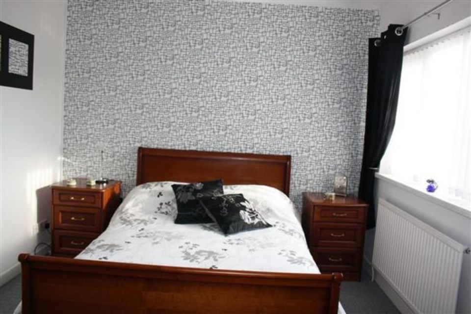 Bedroom with wooden sleigh bed, white floral duvet, black pillows, matching nightstands, and patterned wallpaper.